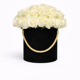 Round box of white roses in a black hatbox with a gold rope handle