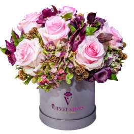 Pink roses and purple flowers arranged in a gray hat box