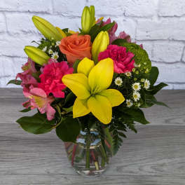 Mixed bouquet with yellow lilies, pink carnations, and an orange rose in a glass vase.