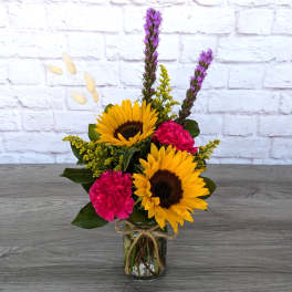 Sunflowers and pink carnations in a glass vase with dried accents