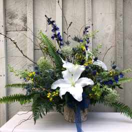 White lilies in a rustic container with blue and yellow flowers
