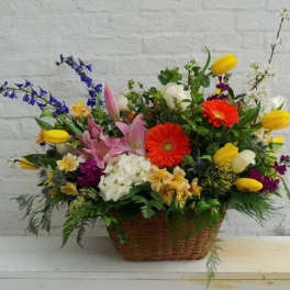 Mixed flower arrangement in a wicker basket with pink, yellow, white, and orange blooms