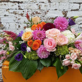 Mixed bouquet of pink, peach, purple, and orange flowers in an orange container