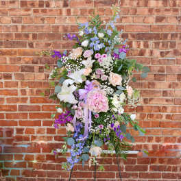 Large pastel floral standing spray with lilies, roses, and purple blooms