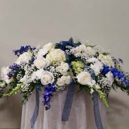 White and blue floral arrangement with ribbon draped over a pedestal