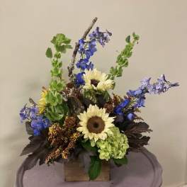 Mixed floral arrangement with sunflowers, blue delphinium, and green hydrangea in a wooden box