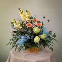 Mixed bouquet in a wooden basket with pale yellow, peach, and blue flowers