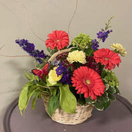 Basket arrangement with pink gerbera daisies, purple flowers, and yellow carnations