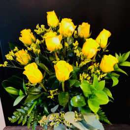 Yellow roses arranged in a clear glass vase with mixed greenery