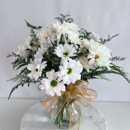 White daisy bouquet in a glass vase with a gold ribbon
