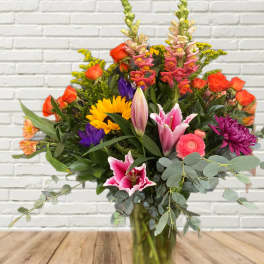 Colorful mixed bouquet in a glass vase with sunflowers, roses, lilies, and snapdragons