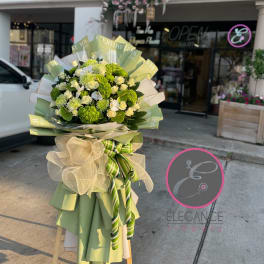 Large bouquet of white and green flowers wrapped in green paper with a bow