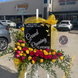 Yellow and pink rose arrangement on an easel sign with gold ribbon