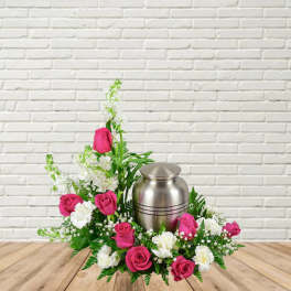 Pink roses and white flowers arranged around a silver urn