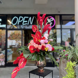 Tall arrangement of red anthuriums and pink flowers in a metallic vase