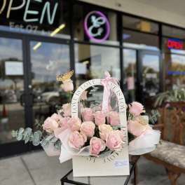 Pink roses arranged in a white basket with a LOVE ribbon