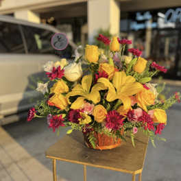 Yellow lilies and roses with magenta daisies in a basket arrangement