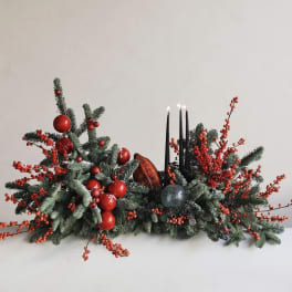 Low holiday centerpiece with evergreen branches, red berries, and black candles