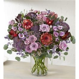 Lavender roses and purple flowers in a clear glass vase