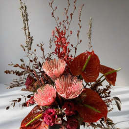 Tall floral arrangement with red anthuriums and pink protea in a black vase