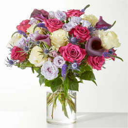Bouquet of pink and cream roses with purple accents in a clear glass vase