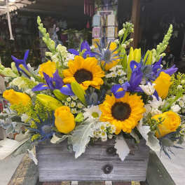 Mixed bouquet with sunflowers, yellow roses, and blue irises in a wooden box