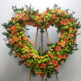 Heart-shaped floral wreath of orange roses and green pompons on an easel