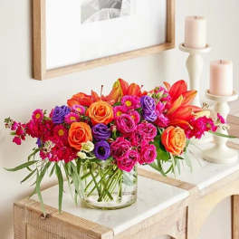 Bright mixed bouquet in a clear glass vase beside two candles