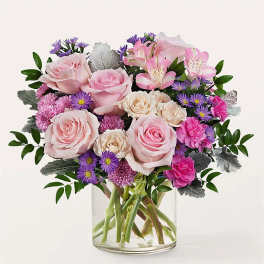 Bouquet of pink roses, alstroemeria, and purple daisies in a clear glass vase