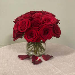 Red rose bouquet in a clear glass vase with rose petals on the table