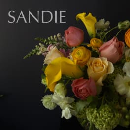Bouquet of yellow calla lilies, roses, and white flowers against a dark background