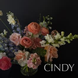 Mixed bouquet of peach, pink, white, and blue flowers in a glass vase