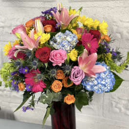 Colorful mixed bouquet in a tall red vase with roses, lilies, hydrangeas, and daisies