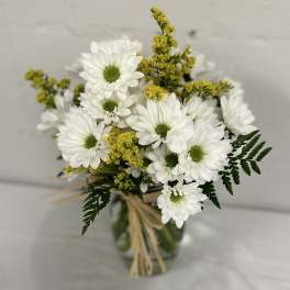 White daisy bouquet with yellow filler in a glass vase