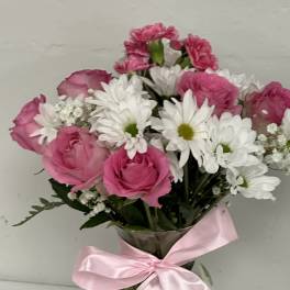 Pink roses and white daisies in a clear vase with a pink ribbon
