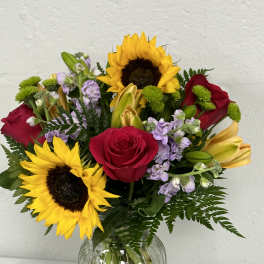 Bouquet of sunflowers, red roses, and lilies in a glass vase