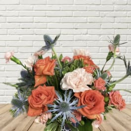 Orange and blush roses with blue thistle in a low bouquet