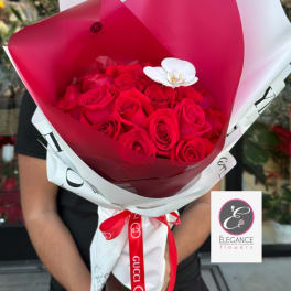 Bouquet of red roses wrapped in white and red paper with a white orchid accent