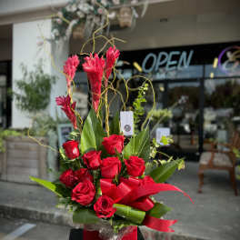 Red roses arranged in a red box with tall pink tropical blooms
