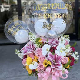 Pink and white floral arrangement with clear balloons and gold lettering