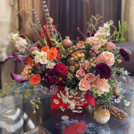 Mixed bouquet with roses, chrysanthemums, and decorative bird accents in a red container