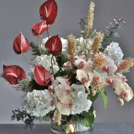 Mixed floral arrangement with red anthuriums, pale orchids, and white hydrangeas in a glass vase