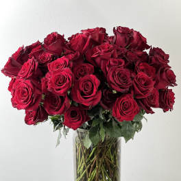 Bouquet of red roses in a clear glass vase with petals around the base