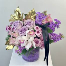 Lavender roses and purple flowers in a glass vase with gold leaves