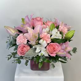 Pink and white bouquet of roses, lilies, carnations, and alstroemeria in a pink glass cube vase