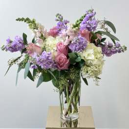 Pink roses and purple blooms in a clear glass vase