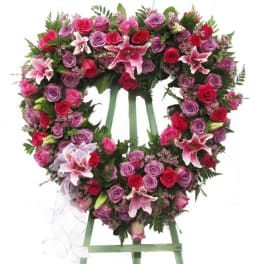Heart-shaped floral wreath on a stand with pink and red roses and lilies