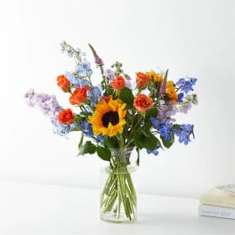 Mixed bouquet with a sunflower and orange roses in a clear glass vase