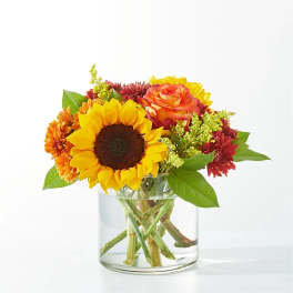 Sunflower and mixed autumn flowers in a clear glass vase