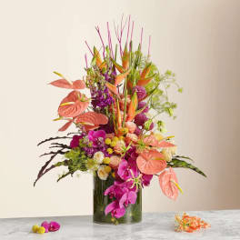 Tall tropical arrangement in a glass vase with pink anthuriums and orchids